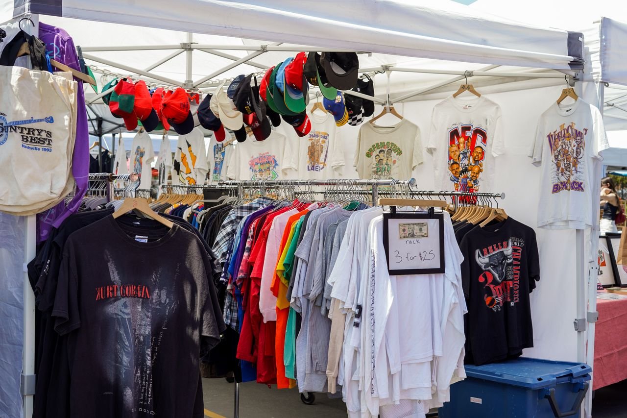 A vibrant street market stall featuring a variety of colorful t-shirts and caps under a tent.